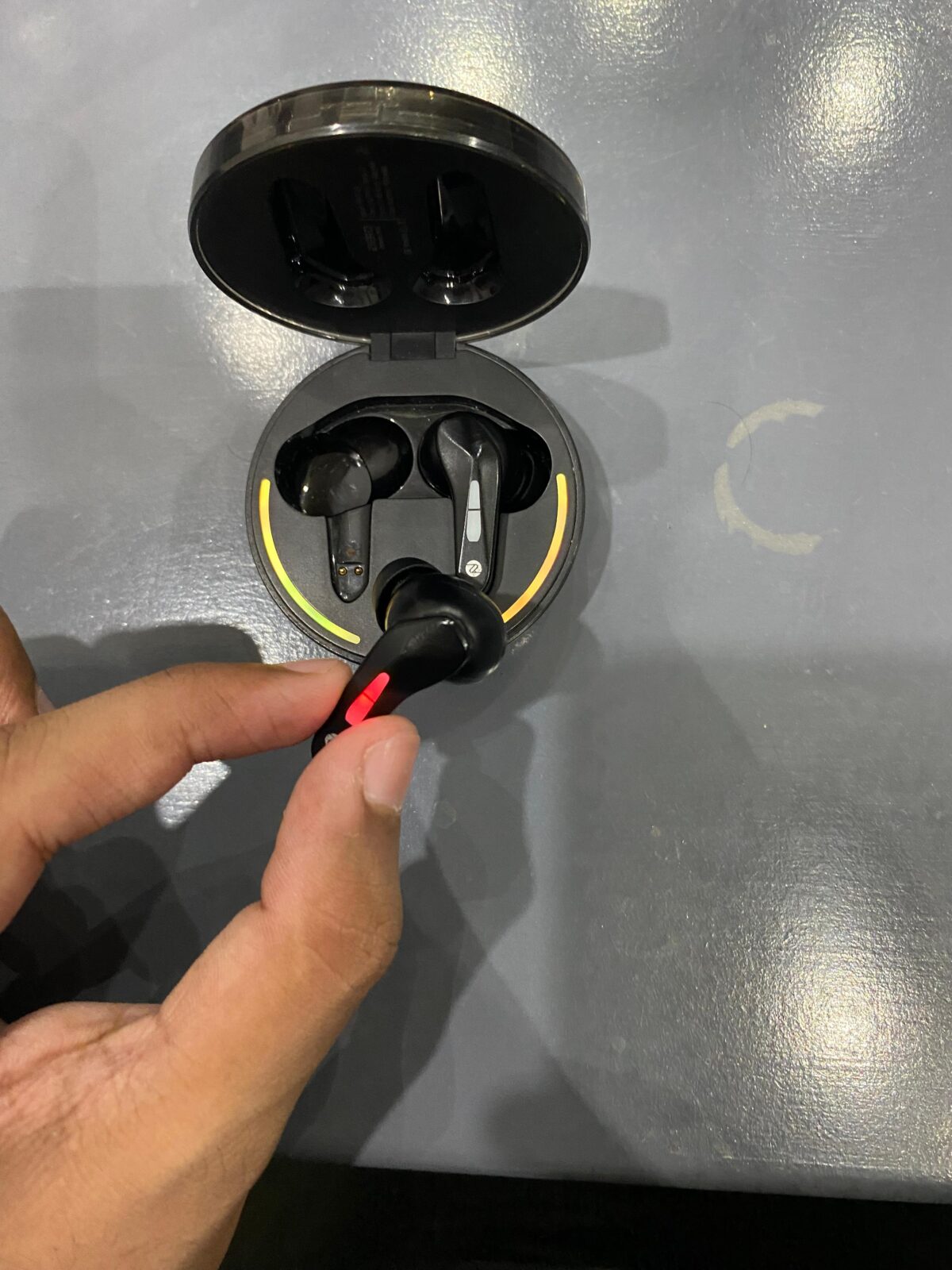 A close-up showing a finger pressing the touch-sensitive control zone beneath the RGB LED strip on the Zero Arcade 900 earbud.