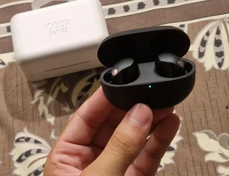Hand holding black Sony WF-1000XM5 earbuds in an open charging case.