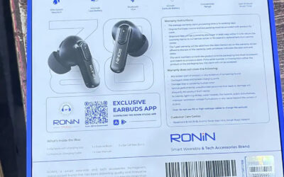 Ronin-R-860-TWS-earbuds-inside-their-matte-black-charging-case-resting-on-a-wooden-developer-desk-next-to-a-mechanical-keyboard