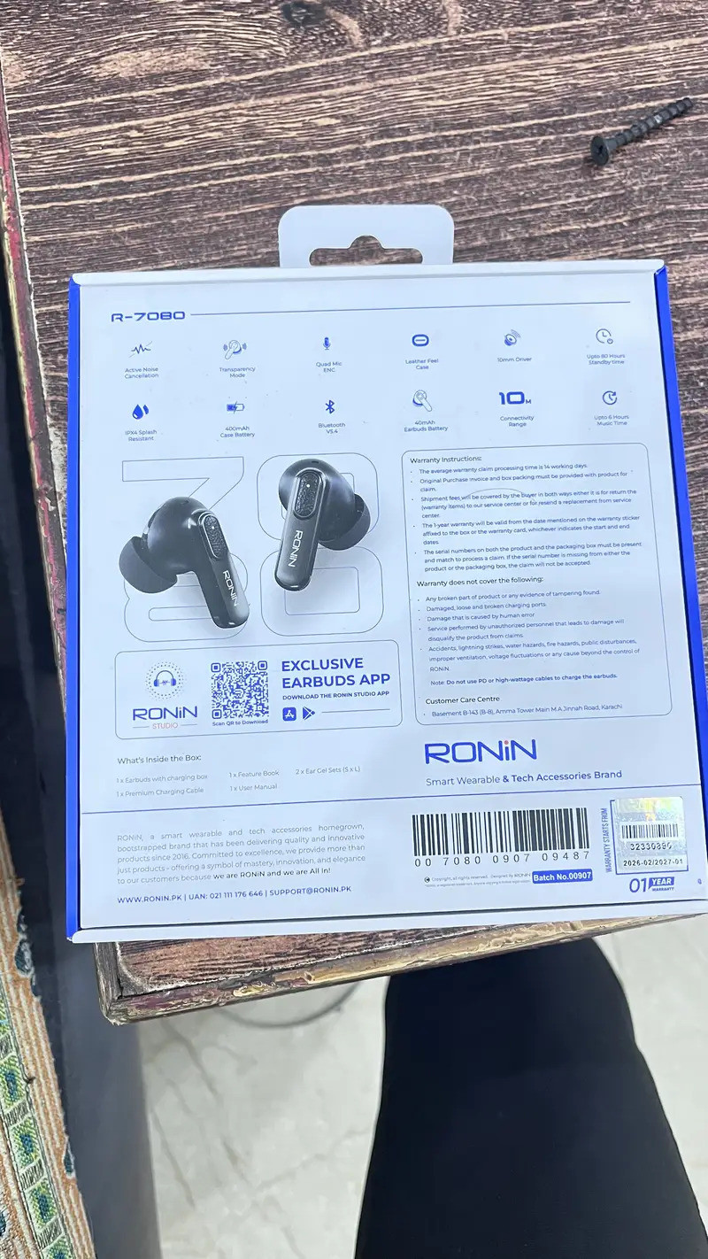 Ronin R-860 TWS earbuds inside their matte black charging case resting on a wooden developer desk next to a mechanical keyboard.